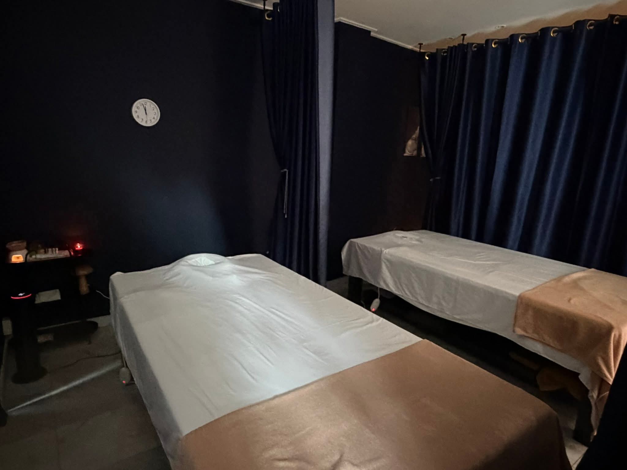Behandelkamer in gedimd licht met twee massagetafels en een klok aan de muur