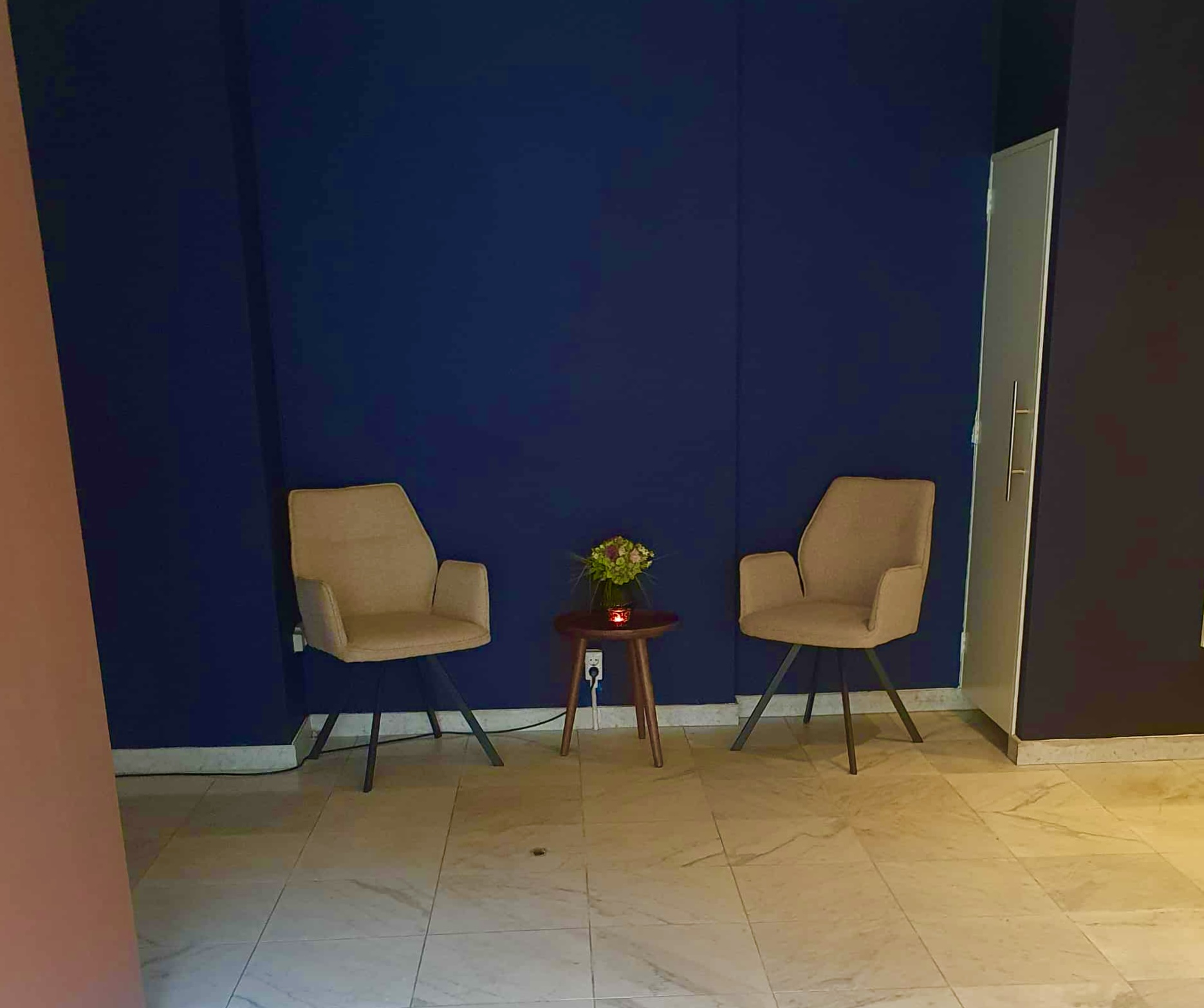 Twee beige stoelen met een bijzettafeltje tegen een donkerblauwe muur