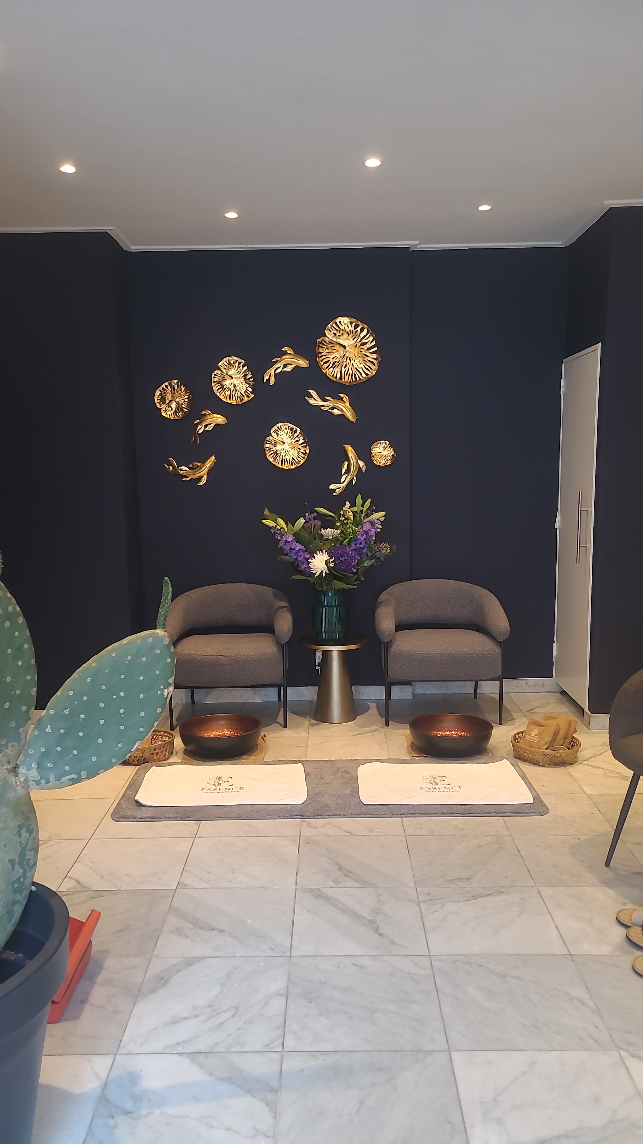 Wachthoek met twee grijze stoelen, gouden bladeren aan de donkerblauwe muur, koperen voetbaden en een cactus